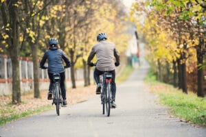 A rear view of senior couple with electrobikes cycling outdoors on a road.